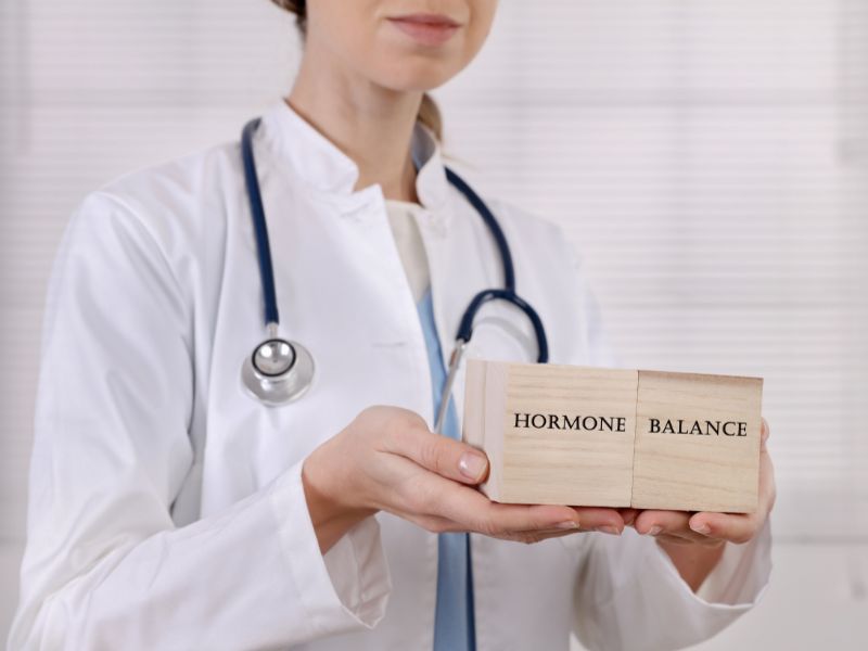 Female doctor with lab coat holds two wooden blocks with the words hormone balance
