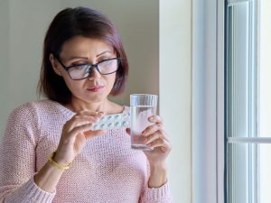 middle-aged woman trying to treat menopausal symptoms with pills and water
