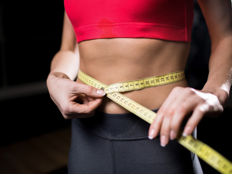 woman with tape measure around waist to illustrate satisfaction after using weight loss medications