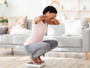 young black woman on scales looking shocked at weight gain after hysterectomy