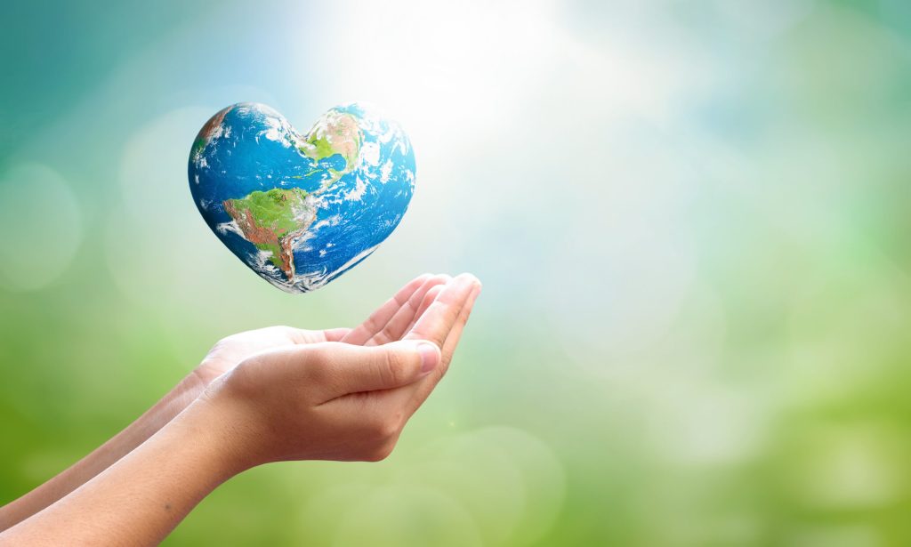 World environment day concept: man opens palms and drags heart shaped earth globe over blurred blue sky and water background. Elements of this image furnished by NASA. To illustrate root-cause healthcare